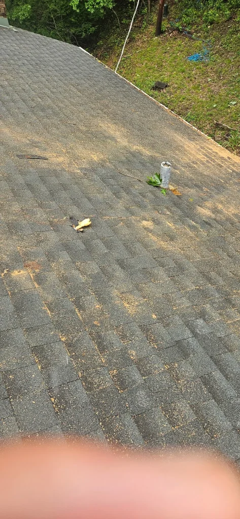 A gray shingled roof is covered in sawdust and small debris with a metal vent pipe visible